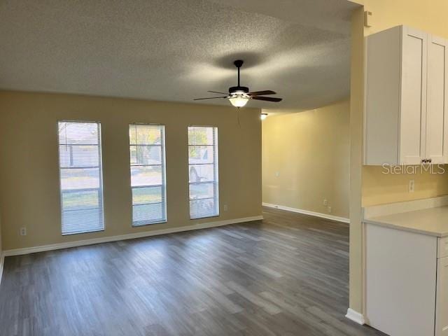 unfurnished living room with dark wood finished floors, ceiling fan, a textured ceiling, and baseboards