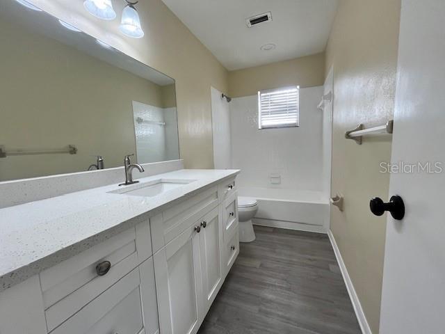 bathroom featuring visible vents, toilet, wood finished floors, vanity, and shower / bathtub combination