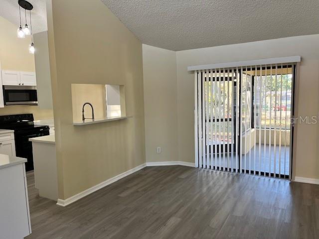 unfurnished living room with high vaulted ceiling, a sink, a textured ceiling, baseboards, and dark wood-style flooring