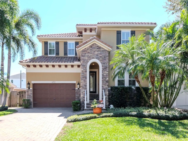 mediterranean / spanish-style home featuring a front yard, stucco siding, stone siding, a tiled roof, and decorative driveway