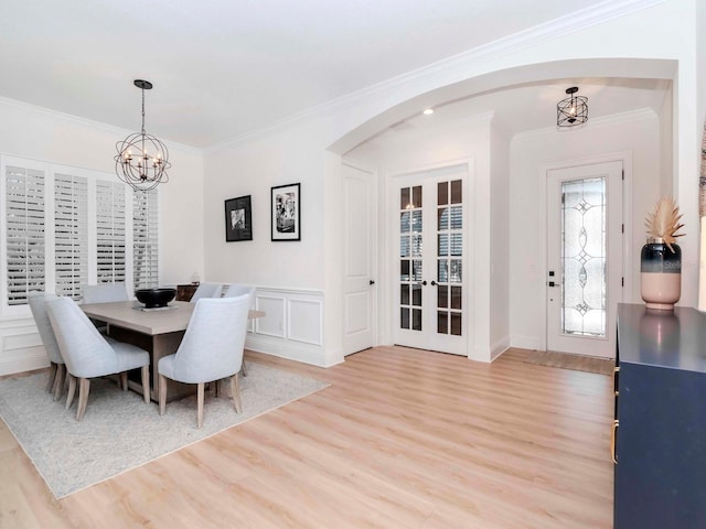 dining space featuring arched walkways, light wood-style floors, crown molding, a decorative wall, and a chandelier