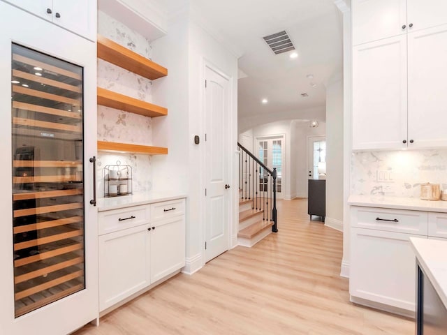 bar featuring visible vents, backsplash, beverage cooler, light wood-style flooring, and arched walkways