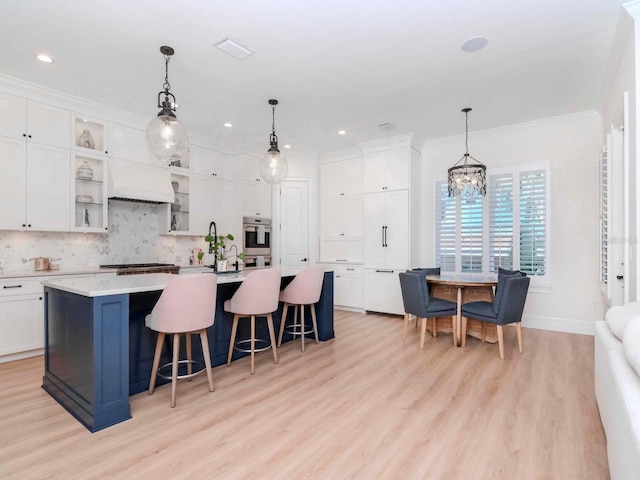 kitchen featuring white cabinetry, an island with sink, backsplash, and ornamental molding