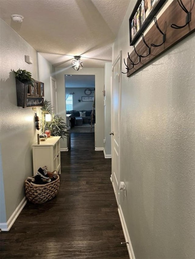 hall with a textured wall, baseboards, dark wood-type flooring, and a textured ceiling