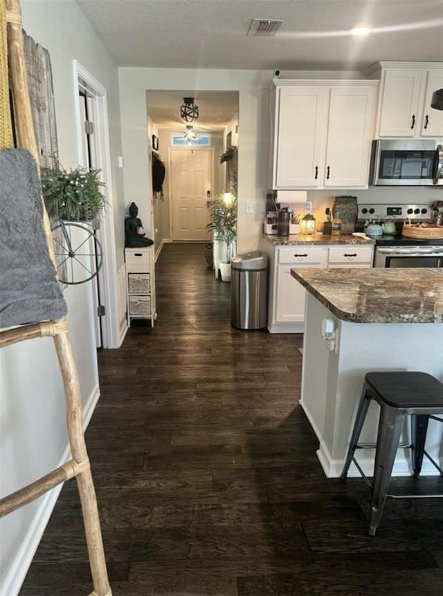 kitchen featuring stainless steel appliances, visible vents, white cabinets, and dark wood-style flooring