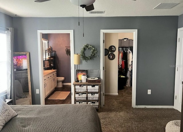 carpeted bedroom featuring a walk in closet, visible vents, a textured ceiling, ensuite bath, and a closet