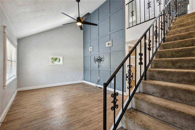 stairs with visible vents, high vaulted ceiling, a ceiling fan, wood finished floors, and baseboards