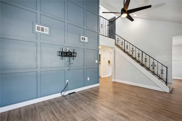 unfurnished living room with ceiling fan, visible vents, wood finished floors, and a decorative wall