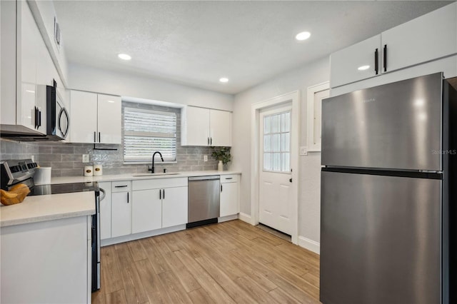 kitchen with light wood-type flooring, a sink, white cabinetry, appliances with stainless steel finishes, and light countertops