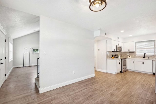 kitchen with light wood finished floors, a sink, light countertops, appliances with stainless steel finishes, and backsplash