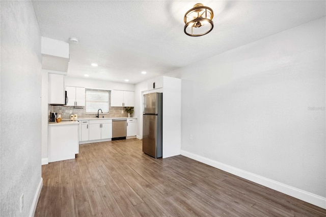 kitchen featuring wood finished floors, a sink, decorative backsplash, light countertops, and appliances with stainless steel finishes