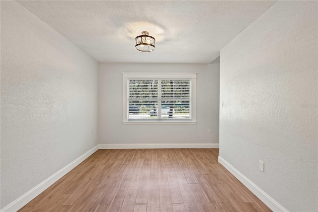 empty room with baseboards, light wood-type flooring, a textured wall, and a textured ceiling