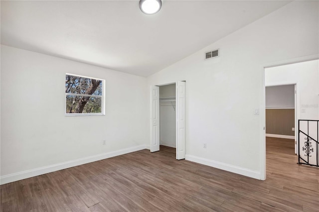 unfurnished bedroom featuring wood finished floors, visible vents, baseboards, lofted ceiling, and a closet