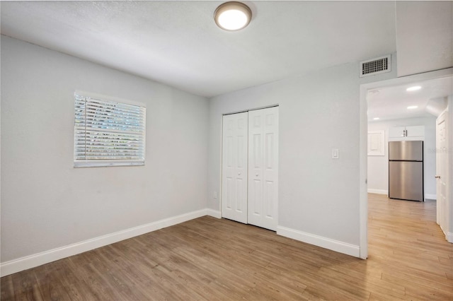 unfurnished bedroom with light wood finished floors, visible vents, freestanding refrigerator, and baseboards