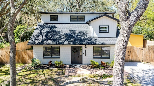 view of front of house featuring brick siding, a shingled roof, and fence