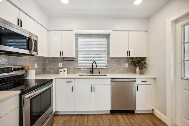 kitchen featuring light countertops, light wood-type flooring, decorative backsplash, appliances with stainless steel finishes, and a sink