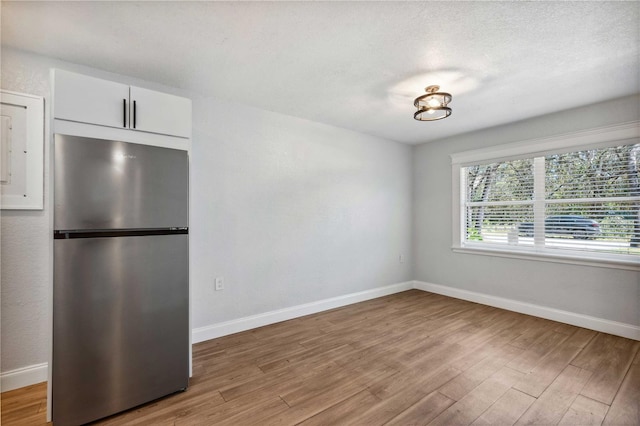 interior space with white cabinets, light wood-style floors, baseboards, and freestanding refrigerator