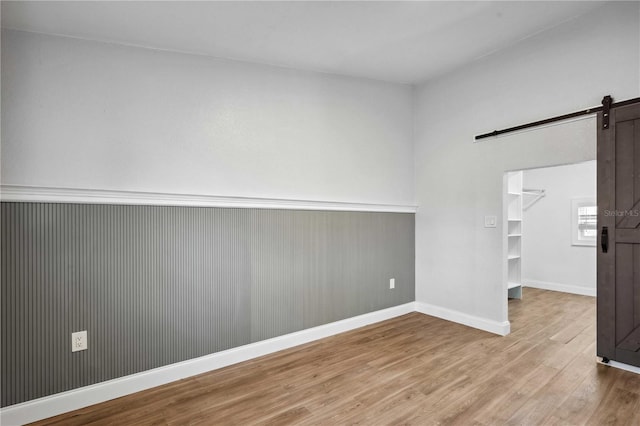 spare room featuring a barn door, wood finished floors, and baseboards