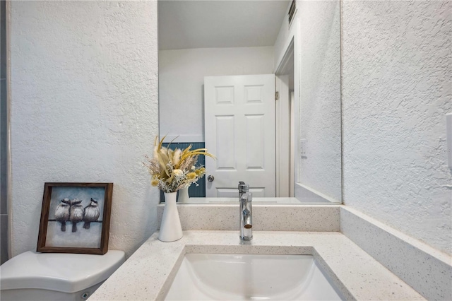 bathroom with visible vents, toilet, vanity, and a textured wall