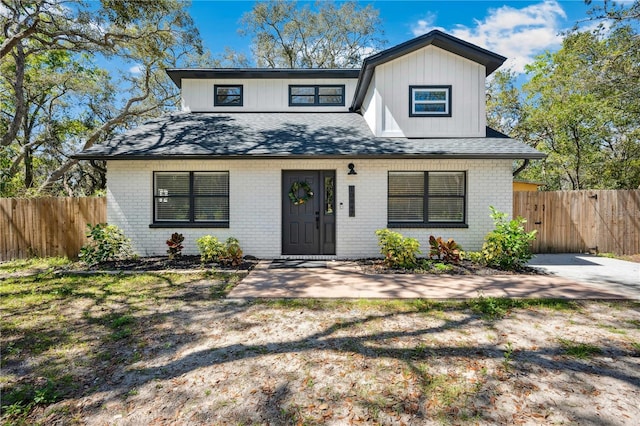 view of front of home featuring fence, brick siding, and roof with shingles