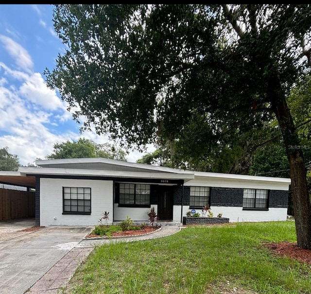 view of front of home with concrete block siding, fence, a front yard, and a carport