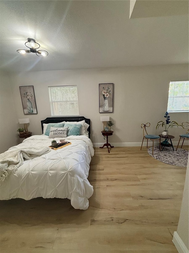 bedroom featuring a textured ceiling, light wood-type flooring, and baseboards