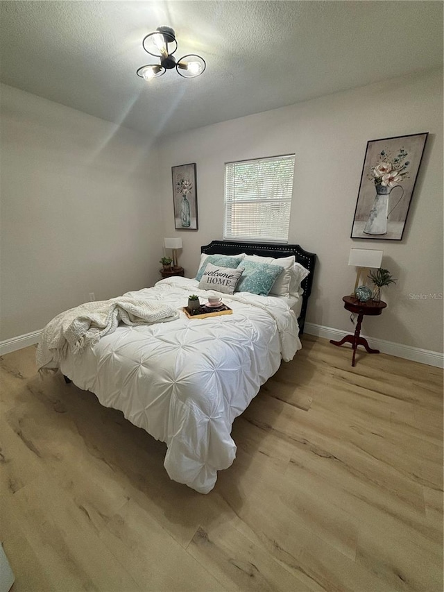 bedroom featuring baseboards, light wood-type flooring, and a textured ceiling