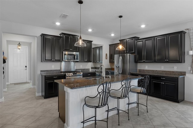 kitchen featuring visible vents, a sink, stainless steel appliances, a breakfast bar area, and dark cabinets