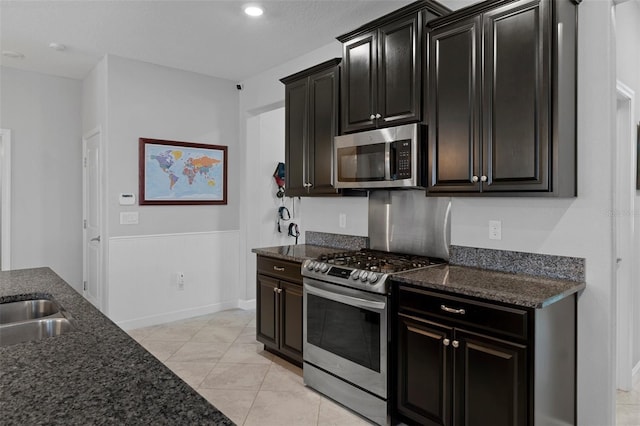 kitchen featuring dark stone countertops, a sink, appliances with stainless steel finishes, light tile patterned flooring, and dark cabinets