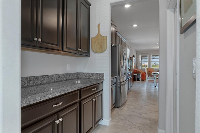 kitchen with stone countertops, recessed lighting, stainless steel fridge with ice dispenser, light tile patterned floors, and dark brown cabinets