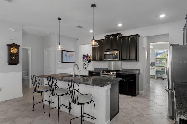 kitchen with visible vents, dark stone counters, a kitchen breakfast bar, stainless steel appliances, and a sink