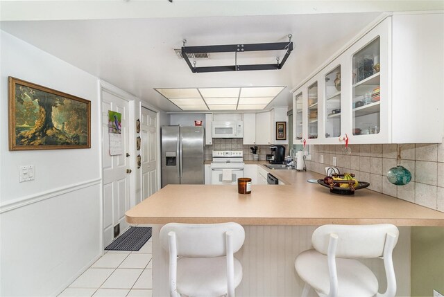 kitchen featuring tasteful backsplash, white appliances, a peninsula, light tile patterned floors, and glass insert cabinets