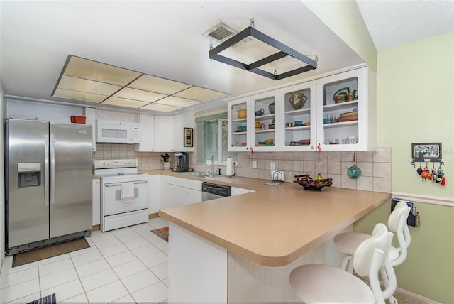 kitchen with a peninsula, stainless steel appliances, decorative backsplash, glass insert cabinets, and white cabinetry