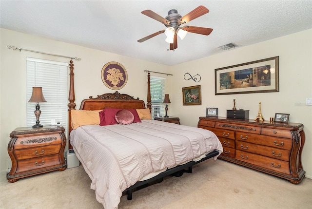 bedroom with a textured ceiling, a ceiling fan, visible vents, and light carpet