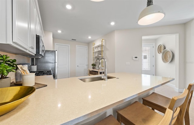 kitchen featuring tasteful backsplash, stainless steel microwave, a peninsula, white cabinetry, and a sink