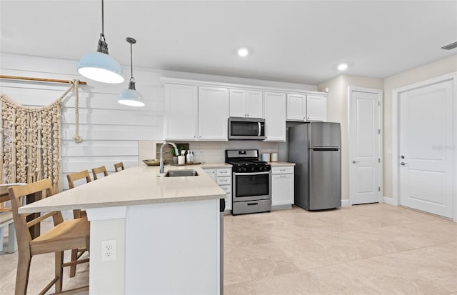 kitchen featuring a kitchen bar, light countertops, appliances with stainless steel finishes, white cabinetry, and a sink