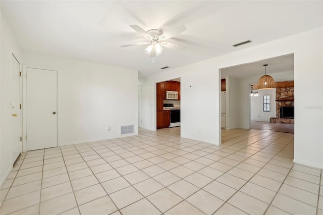 spare room featuring light tile patterned floors, a fireplace, visible vents, and ceiling fan