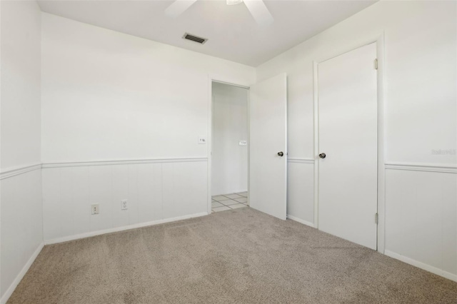 unfurnished bedroom featuring a wainscoted wall, carpet flooring, visible vents, and ceiling fan