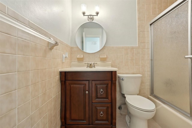 bathroom with toilet, vanity, wainscoting, shower / bath combination with glass door, and tile walls