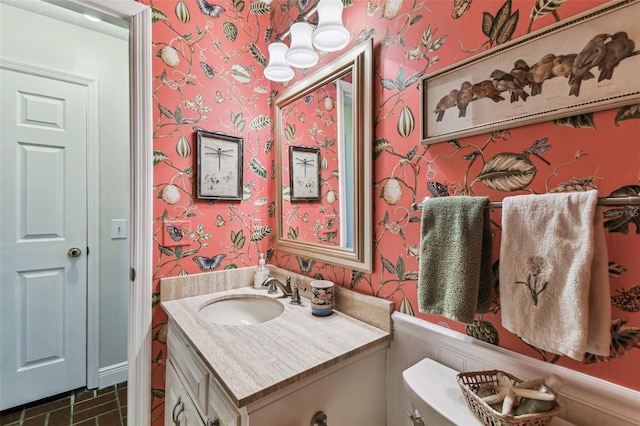 half bathroom featuring wallpapered walls, toilet, and vanity