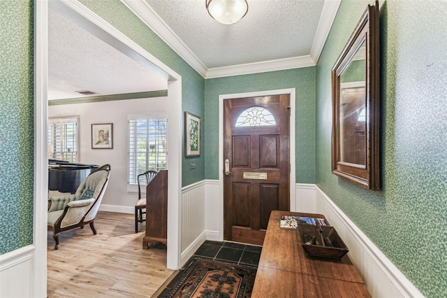 foyer with visible vents, ornamental molding, a textured ceiling, wood finished floors, and wainscoting