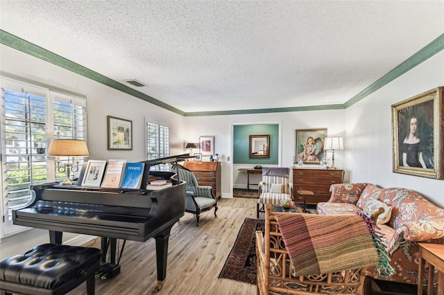 living room featuring wood finished floors, baseboards, visible vents, a textured ceiling, and crown molding