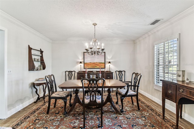 dining room featuring wood finished floors, visible vents, ornamental molding, a textured ceiling, and a notable chandelier