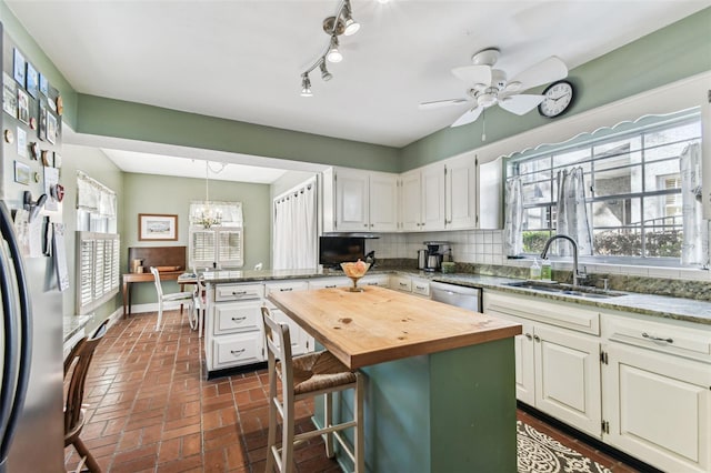 kitchen featuring wooden counters, brick floor, a sink, appliances with stainless steel finishes, and tasteful backsplash