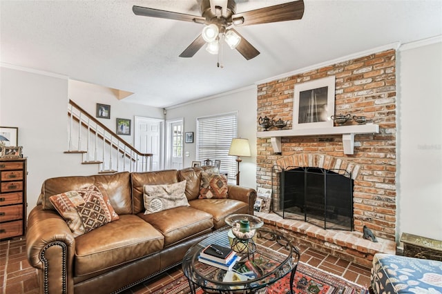 living area featuring stairway, a fireplace, ceiling fan, ornamental molding, and a textured ceiling