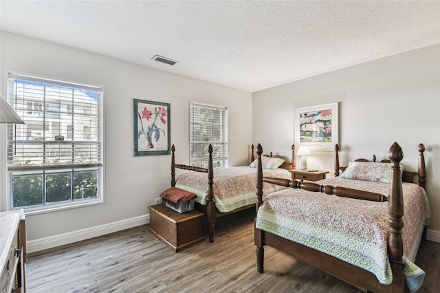 bedroom with multiple windows, wood finished floors, visible vents, and a textured ceiling