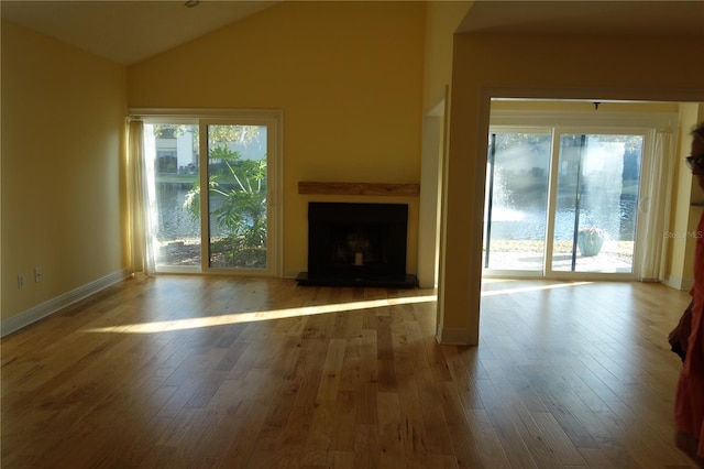 unfurnished living room with wood finished floors, a fireplace with raised hearth, baseboards, and vaulted ceiling