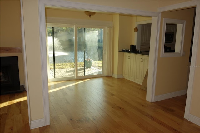 interior space with a fireplace with raised hearth, baseboards, and light wood-style floors