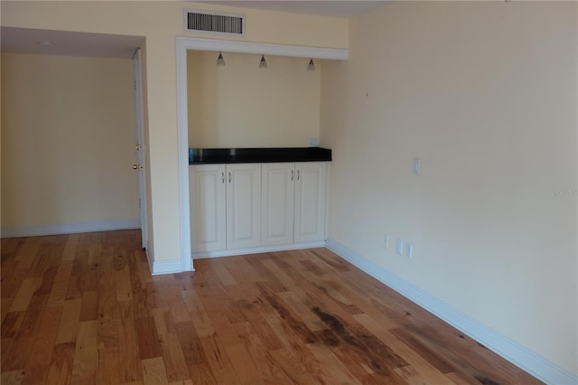 spare room featuring light wood-type flooring, visible vents, and baseboards