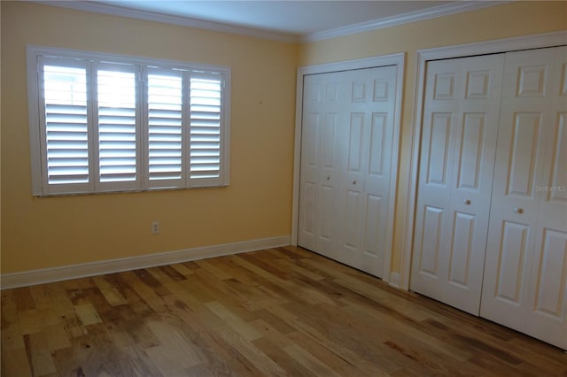 unfurnished bedroom featuring wood finished floors, baseboards, multiple closets, and ornamental molding